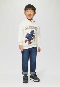 Biała bluza z kapturem z napisem "GAMEDAY" i grafiką dinozaura, w połączeniu z niebieskimi dżinsami i czarnymi sneakersami z limonkowymi akcentami.