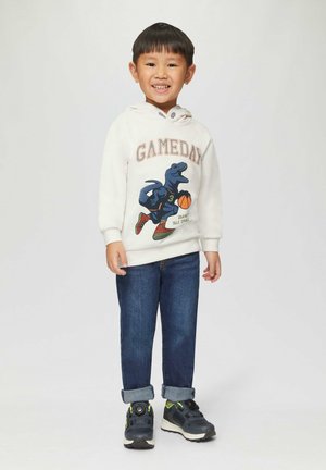 Biała bluza z kapturem z napisem "GAMEDAY" i grafiką dinozaura, w połączeniu z niebieskimi dżinsami i czarnymi sneakersami z limonkowymi akcentami.