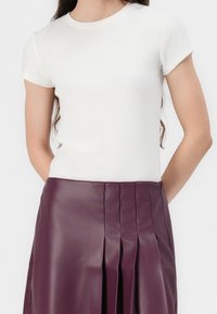 Žena v jednoduchém bílém krátkém rukávu, zasunutém do sukně s vysokým pasem, skládané, z tmavě fialové koženky.