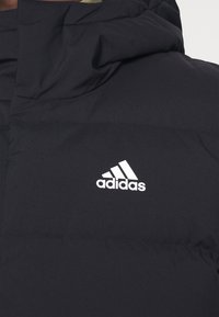 Černá polstrovaná bunda s velkým límcem, na němž je uprostřed hrudníku umístěno bílé logo Adidas.