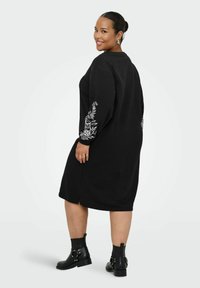 Czarna, oversize sukienka z długimi rękawami, ozdobiona białą kwiatową haftowaną dekoracją na mankietach. Stylizowana z czarnymi botkami na kostkę.