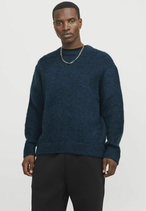 Pulover tricotat bleumarin, cu un finisaj texturat, guler rotund și manșete cu model, asortat cu pantaloni negri. Accent de lanț simplu din argint.