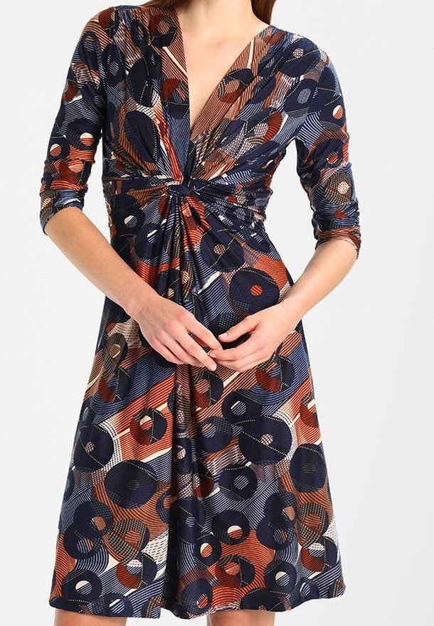 Monivärinen mekko, jossa on syvä V-pääntie, kolmannes hiha ja solmittu etuosa. Kangas sisältää pyöreän kuvion, jossa on laivastonsinistä, oranssia ja valkoista.