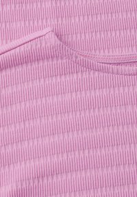 Texturovaná růžová tkanina s vertikálními pruhy a jemným žebrováním. Materiál má měkký vzhled, ukazuje kulatý výstřih a pečlivé šití.