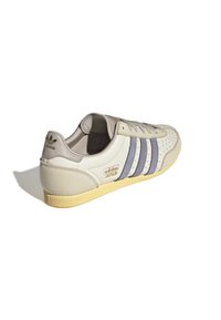 Białe skórzane sneakersy z trzema granatowymi paskami, perforowanym detalem palca, beżowymi akcentami i teksturowaną gumową podeszwą. Branding na pięcie.
