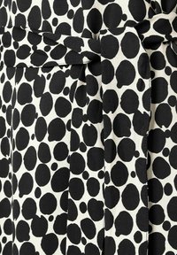 Tissu noir et blanc avec un grand motif à pois, présentant un détail de ceinture nouée et une finition texturée.