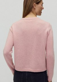 Rosa tröja med rundad halsringning, långa ärmar och kort skärning. Tillverkad av mjukt material med en slät yta och minimal detaljer.