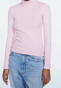 Světle růžový žebrovaný rolák s dlouhým rukávem a přiléhavým střihem, doplněný o casual modré džíny. Měkká textura a elastický materiál.
