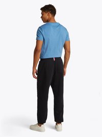 T-shirt in cotone blu abbinata a pantaloni neri con stampa del logo laterale, completata da sneakers chiare, vista da dietro.