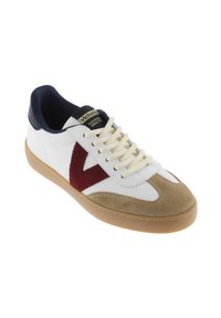 Chaussure de sport blanche avec un talon bleu marine, des accents en daim beige et un logo bordeaux ; elle présente une semelle beige et des lacets tissés.