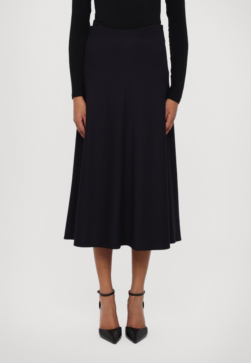 Falda midi negra hecha de tela suave, con un diseño en línea A, una cinturilla ancha y un ligero vuelo. Combinada con tacones negros de punta afilada.