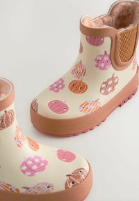 Botas de lluvia de goma rosa y beige con patrones de calabaza, acentos marrones texturizados y un forro de felpa para mayor comodidad.