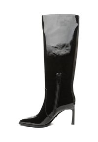 Botas negras de charol hasta la rodilla con punta afilada y tacón de aguja delgado. Cuentan con una cremallera lateral para facilitar su uso.