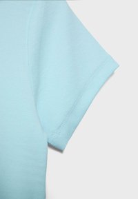 Jasnoniebieska tkanina koszuli z krótkim rękawem, zbliżenie pokazujące szczegóły szwu na końcu rękawa na jednolitym tle.