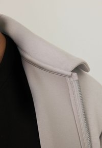 Light gray hoodie with a folded collar and zipper detail, paired with a black fabric underneath. Smooth texture and casual design.