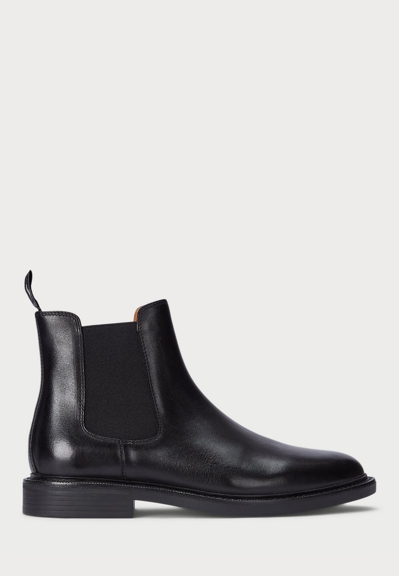 Botte Chelsea en cuir noir avec panneau latéral élastique, languette arrière et petit talon empilé sur fond uni gris clair.