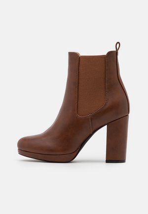 Hnědá kožená kotníková bota s elastickými bočními panely, zaoblenou špičkou a vysokým blokovým podpatkem. Hladký povrch s elegantním designem.