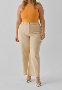 Pantalones anchos beige con bolsillos laterales y una tela suave, combinados con una blusa ajustada de color naranja brillante y zapatos de tacón alto plateados.