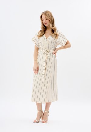 Robe enveloppante couleur crème avec des rayures verticales noires, des manches larges, une ceinture nouée à la taille et une longueur midi. Assortie avec des talons lanières.