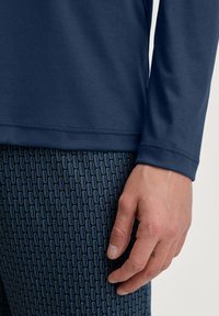 Marineblaue Langarmbluse mit glatter Textur, kombiniert mit gemusterten Leggings, die ein geometrisches Design in Blautönen aufweisen.