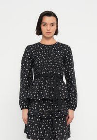 Robe noire à fleurs avec manches longues, corsage smocké, design à basque et ceinture assortie. Présente des motifs floraux crème et pastel.