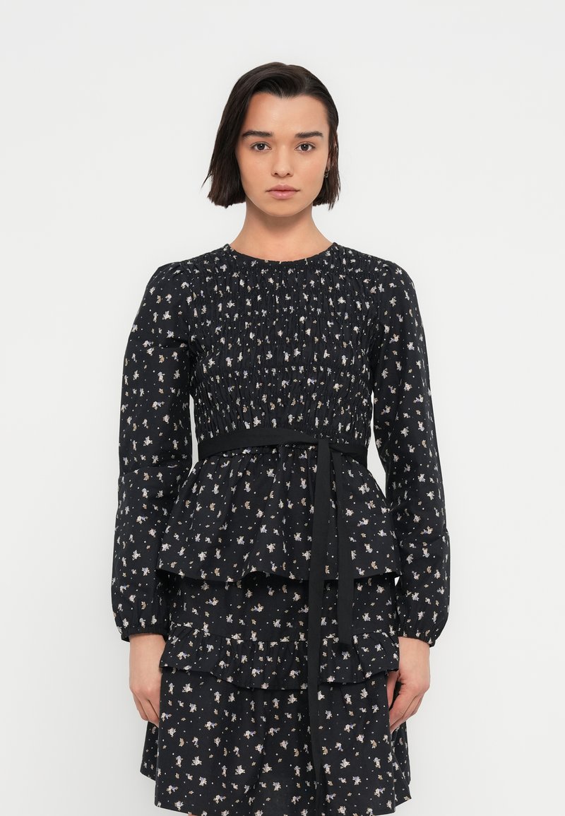 Robe noire à fleurs avec manches longues, corsage smocké, design à basque et ceinture assortie. Présente des motifs floraux crème et pastel.