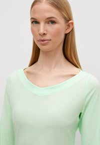 Top a maniche lunghe verde menta con scollatura a V ampia, realizzato in tessuto morbido, con una superficie liscia e dettagli di cuciture minime.