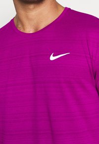 Hombre vistiendo una camiseta deportiva de Nike de un brillante color púrpura, con el logo blanco de la marca en la parte superior del pecho.
