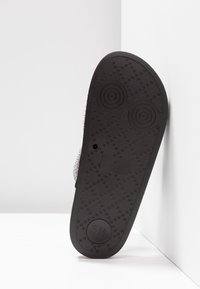 Semelle de chaussure en caoutchouc noir avec un motif de texture antidérapant. Présente des accents circulaires et la taille imprimée "US 7".