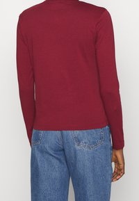 Burgunderrotes Langarmshirt aus Baumwolle, mit taillierter Passform und Rundhalsausschnitt, kombiniert mit hellblauen Jeans.