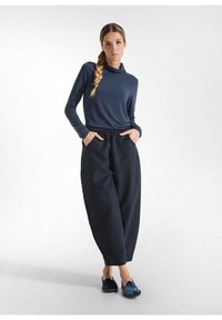 Cămașă albastră cu mânecă lungă și guler cowl; pantaloni largi, închiși la culoare, cu buzunare; material moale; pantofi slip-on, textura închisă.