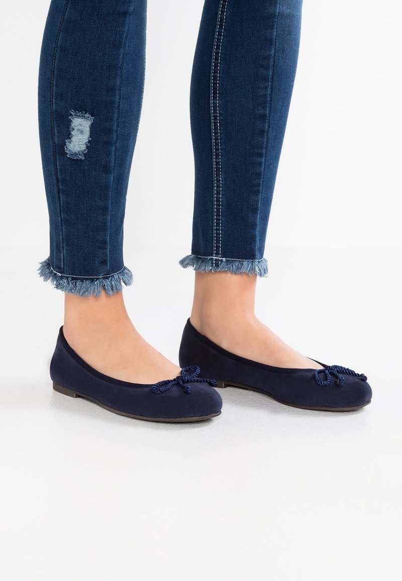 Navyblå ballerinaskor i mjukt material, med rund tå, dekorerad rosett och låg profil. Bärs med fransade ankellånga jeans.
