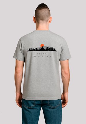 Man facing away wearing a gray t-shirt with a black mountain skyline and orange sun design above the word "ESCAPE" and smaller text below.
