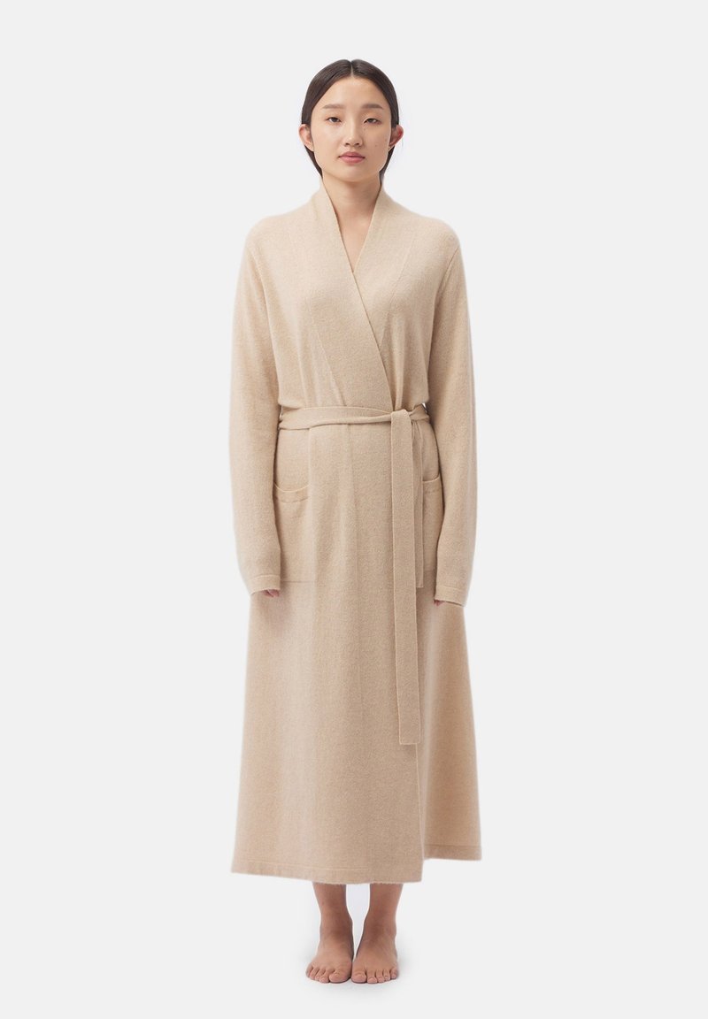 Robe longue beige en tissu doux ; dotée d'un col châle, de manches longues, d'une ceinture à nouer et de deux poches avant. Texture lisse, coupe jusqu'au sol.