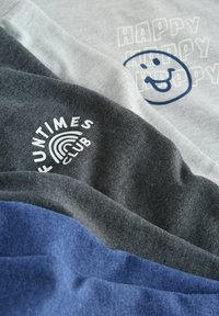 Złożony niebieski, ciemnoszary i jasnoszary materiał z nadrukowanymi wzorami, w tym "FUNTIMES CLUB" oraz uśmiechniętą twarzą z napisem "HAPPY".