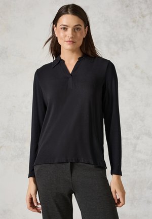 Schwarzes Langarm-Polo-Shirt mit V-Ausschnitt, glatter Textur und seitlichen Schlitzen, kombiniert mit dunkelgrauen Hosen.