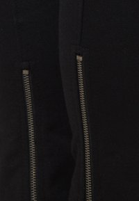 Zwarte leggings met zijkanten van ritsen met metalen hardware, een gladde stofstructuur, een strakke pasvorm en contrasterende stikseldetails.