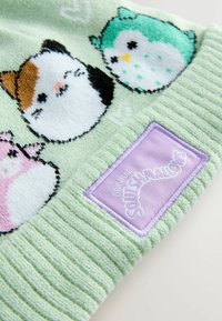 Vihreä fleece-hattu, jossa on pastellisävyisiä sarjakuvahulmuja eläindesigneja, ribbitekstuuri ja violetti kangaslabeli, jossa lukee "Original Squishmallows".