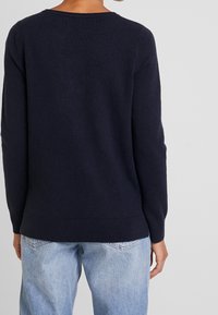Pull bleu marine en tricot doux, avec un col rond, des manches longues et des poignets et ourlet côtelés pour un ajustement confortable.