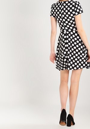 Mustavalkoinen pilkullinen mekko, jossa on lyhyet hihat, liehuhame ja istuva yläosa. Yhdistetty mustiin korkokenkiin.