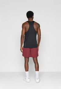 Čierny bezrukávový športový nátelník a vínové šortky. Nátelník má pretekársky strih, zatiaľ čo šortky sú po kolená a majú bočné vrecká.