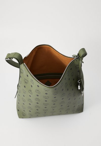 Green leather handbag with black MCM logos, open top zipper, tan suede interior, and adjustable shoulder strap with silver hardware.