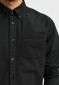 Camisa negra de botones hecha de algodón. Presenta un cuello clásico, bolsillo en el pecho y botones oscuros. Textura suave con un corte entallado.