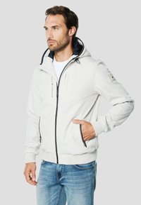 Helehall zip-up dress, millel on kapuuts, kontrastne tumesinine vooder, ees taskud, soonilised varrukasäärised ja tikitud logoga detail. Kandmisega siniste teksapükstega.