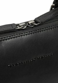 Schwarze Lederhandtasche mit glatter Textur, ausgestattet mit silberfarbenen Metallteilen, einem Reißverschluss und einem eingeprägten Logodetail. Klare Linien und minimalistisches Design.