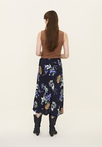 Un top maro fără mâneci, asortat cu o fustă florală bleumarin cu modele verzi și mov, completat de cizme negre de tip cowboy.