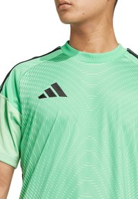 Grünes Sportshirt mit kurzen Ärmeln, ausgestattet mit dem schwarzen Adidas-Logo, einem strukturierten Mustedesign und kontrastierenden schwarzen Schulterstreifen.