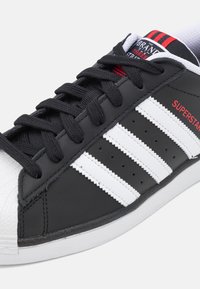 Czarne skórzane sneakersy z białym wzorem w trzy paski, ozdobione czerwonym tekstem, z klasycznym gumowym czubkiem i czarnymi sznurówkami.