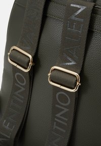 Dark green textured leather backpack with gold-tone hardware; features wide straps embossed with "VALENTINO" in a contrasting finish.