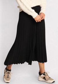 Sort plisseret midi-nederdel med en glat tekstur, parret med beige og sorte sneakers med snørebånd og en polstret sål.